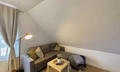 Wohnbereich mit bequemer Eckcouch, Couchtisch, Sessel, Stehlampe, 32-Zoll-Smart-TV, Bluetooth-Radio, Sideboard sowie eine Spielesammlung und kleine Auswahl an Büchern