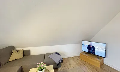 Wohnbereich mit bequemer Eckcouch, Couchtisch, Sessel, Stehlampe, 32-Zoll-Smart-TV, Bluetooth-Radio, Sideboard sowie eine Spielesammlung und kleine Auswahl an Büchern