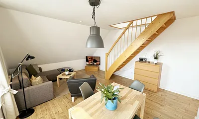 Wohnbereich mit bequemer Eckcouch, Couchtisch, Sessel, Stehlampe, 32-Zoll-Smart-TV, Bluetooth-Radio, Sideboard sowie eine Spielesammlung und kleine Auswahl an Büchern