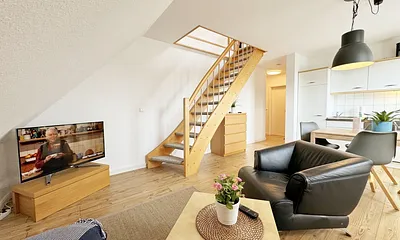 Wohnbereich mit bequemer Eckcouch, Couchtisch, Sessel, Stehlampe, 32-Zoll-Smart-TV, Bluetooth-Radio, Sideboard sowie eine Spielesammlung und kleine Auswahl an Büchern