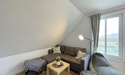 Wohnbereich mit bequemer Eckcouch, Couchtisch, Sessel, Stehlampe, 55-Zoll-Smart-TV, Bluetooth-Radio, Sideboard sowie eine Spielesammlung und kleine Auswahl an Büchern