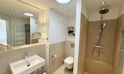 Badezimmer mit bodentiefer Echtglasdusche, Kosmetikspiegel, Fön, Handtuchtrockner sowie einer Lichtkuppel, die diesen Raum schon ab dem frühen Morgen erhellt