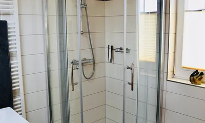 Badezimmer mit Eckrunddusche und Handtuchtrockner über Fußbodenheizung