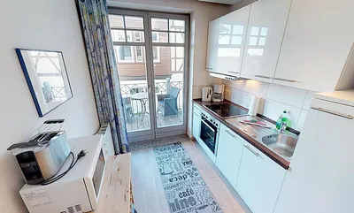 Die voll eingerichtete Küche der Wohnung Kuckuck, dahinter der Balkon, von dem aus Sie das Achterwasser sehen können.