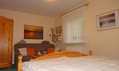 Wohnbereich mit Kleiderschrank, Sofa (ggf. ausklappbar zur Doppelbettcouch bei Aufbettung für max. 1 Pers.), kleinem Tisch und Sessel und Wandboard