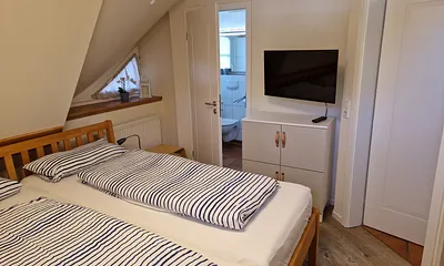 Schlafzimmer 1 im 1. OG mit Doppelbett, angrenzendem Duschbad und TV