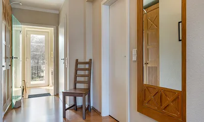 Blick durch den Flur mit Kleiderschrank zum Eingangsbereich. Rückwärtig tritt man aus der Wohnung auf einen überdachten Laubengang/Gemeinschaftsbalkon.