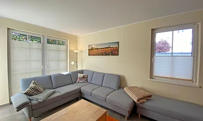 Wohnzimmer mit gemütlicher Eck- Couch mit Hocker, Couchtisch, Stehlampe, zwei Vitrinen, TV-Board mit Flachbild-TV sowie DVD-Player und CD-Player