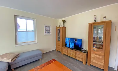 Wohnzimmer mit gemütlicher Eck- Couch mit Hocker, Couchtisch, Stehlampe, zwei Vitrinen, TV-Board mit Flachbild-TV sowie DVD-Player und CD-Player