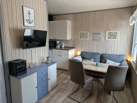 Wohnbereich mit Couch, Esstisch, offener Küche, Fernseher und DVD-Player