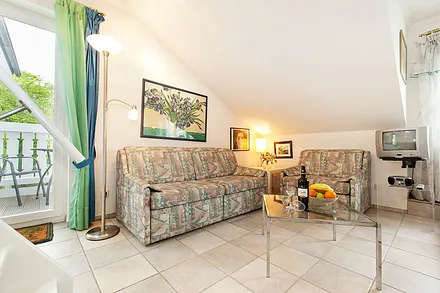 Blick in den Wohnbereich und zum Austritt zum Balkon. Couch und Sessel können für die Aufbettung ausgezogen werden.