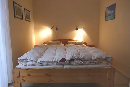Schlafzimmer mit Doppelbett, Schrank, Korbstuhl, Spiegel