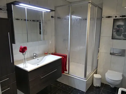 Duschbad mit Dusche (100x100), Toilette, Handtuchhalter, 3D Spiegel, Waschbecken, Schrank für mitgebrachte Gegenstände, Fön, Schminkspiegel, Hocker mit Schmutzwäschebehälter, Personenwaage