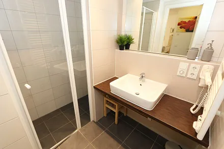 Badezimmer mit ebenerdiger Dusche, Waschbecken, WC, Kosmetikspiegel, festinstallierter Haarfön und Handtuchheizkörper