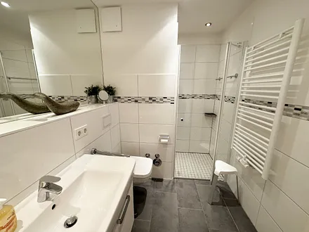 Badezimmer mit ebenerdiger Dusche, Waschbecken, Kosmetikspiegel, Fön, WC und Handtuchheizkörper