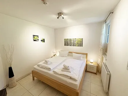 Schlafzimmer mit komfortablem Doppelbett (1,80 m x 2,00 m), hochwertigen Matratzen, Nachttischkonsolen, 4-trg. Drehtürenkleiderschrank (Kernbuche mit Lack creme Fronten), Verdunklungsplissees & TV