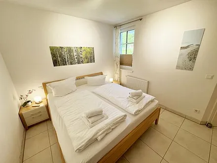 Schlafzimmer mit komfortablem Doppelbett (1,80 m x 2,00 m), hochwertigen Matratzen, Nachttischkonsolen, 4-trg. Drehtürenkleiderschrank (Kernbuche mit Lack creme Fronten), Verdunklungsplissees & TV