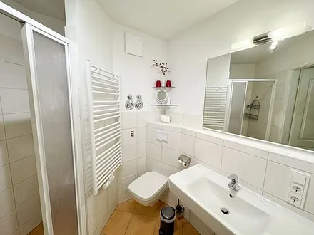 Badezimmer mit ebenerdiger Dusche, Waschbecken, WC und Handtuchtrockner