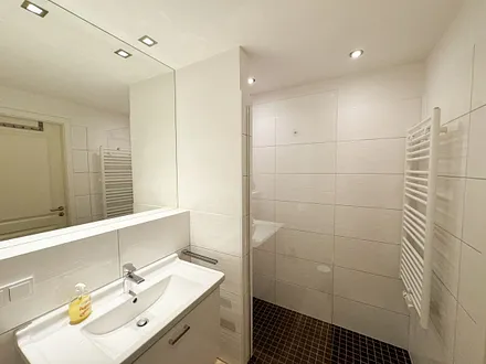 Badezimmer mit ebenerdiger Dusche, Waschbecken, WC und Handtuchheizkörper