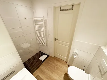 Badezimmer mit ebenerdiger Dusche, Waschbecken, WC und Handtuchheizkörper