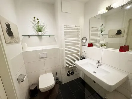 Badezimmer mit ebenerdiger Glasdusche, Fön, Waschbecken, WC und Handtuchtrockner