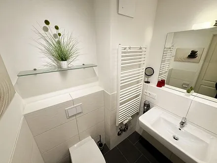 Badezimmer mit ebenerdiger Glasdusche, Fön, Waschbecken, WC und Handtuchtrockner