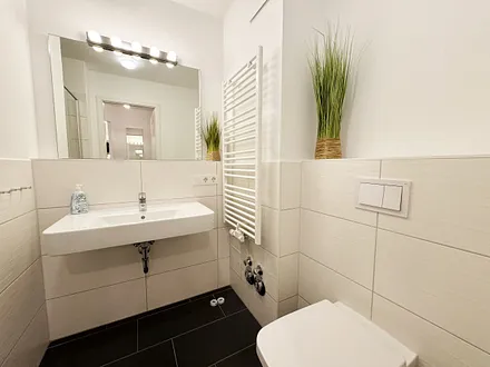 Badezimmer mit ebenerdiger Klarglasdusche, Waschtisch, WC, Fön und Handtuchheizkörper 