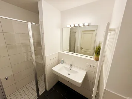 Badezimmer mit ebenerdiger Klarglasdusche, Waschtisch, WC, Fön und Handtuchheizkörper 