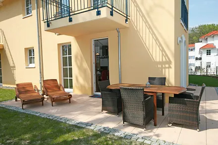 Eckterrasse (Süd/Ost) mit 2 Teakholzliegen und ein Ensemble mit Tisch und vier Stühlen und einem Blick auf die Ostsee durch lichte Baumkronen hindurch