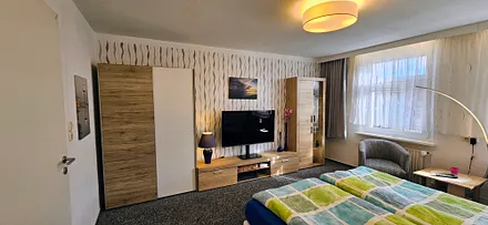 1. Schlafzimmer mit kleiner Anbauwand, Kleiderschrank, Sat-TV,  2 Clubsessel und Tisch, Verducklungsvorhang 