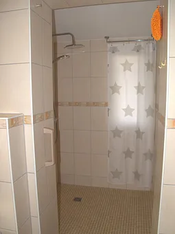 Die begehbare Dusche hat eine Regenbrause. Ein Badhocker steht zur Verfügung 