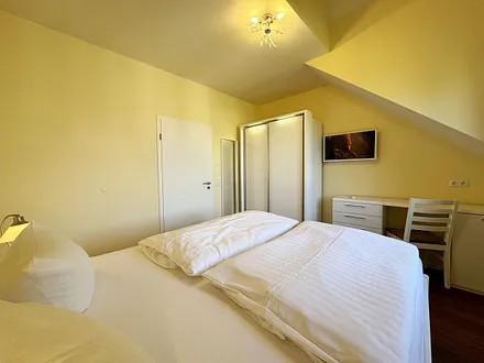 Schlafzimmer mit Doppelbett (1,80 m x 2,00 m mit Komforthöhe), Nachttischablagen, Kleiderschrank, Schreibtisch und Flachbild-TV