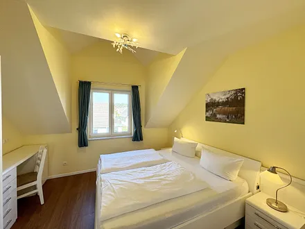 Schlafzimmer mit Doppelbett (1,80 m x 2,00 m mit Komforthöhe), Nachttischablagen, Kleiderschrank, Schreibtisch und Flachbild-TV