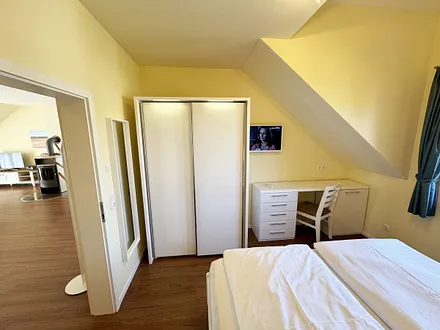 Schlafzimmer mit Doppelbett (1,80 m x 2,00 m mit Komforthöhe), Nachttischablagen, Kleiderschrank, Schreibtisch und Flachbild-TV