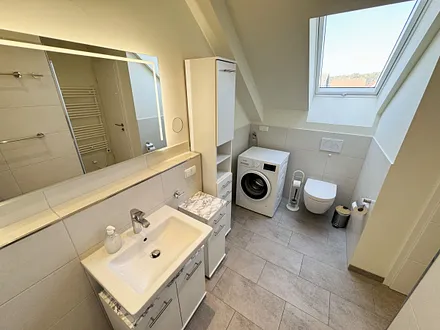 Tageslichtbadezimmer mit ebenerdiger Glasdusche, Waschtisch, WC, Waschmaschine, Kosmetikspiegel, Fön und beheizbarem Handtuchtrockner