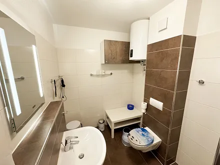 Badezimmer mit Dusche, WC, Kosmetikspiegel, Fön, Waschbecken und Handtuchwärmeheizkörper