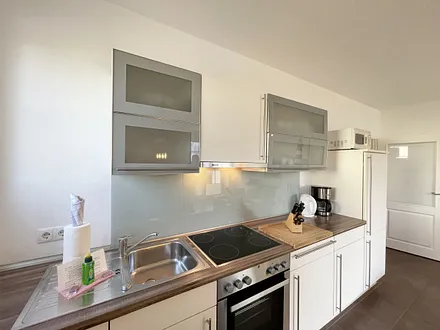 Küchenzeile mit Cerankochfeld, Backofen, Dunstabzugshaube, Kühlschrank mit Gefrierfach, Spülmaschine, Kaffeemaschine, Mikrowelle, Wasserkocher, Toaster und diverse Küchenutensilien