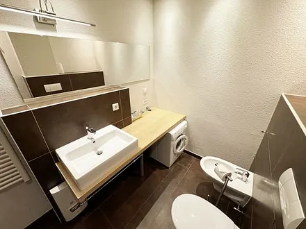 Badezimmer mit bodengleicher Dusche, Waschtisch, WC, Bidet, Handtuchheizung, Waschmaschine (AEG Lavamat), Spiegelleuchte und Fön