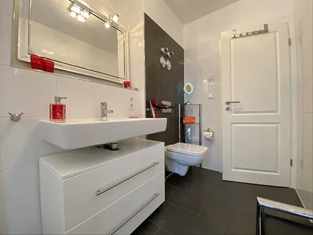 Badezimmer mit ebenerdiger Glasdusche, WC, beheizbaren Handtuchhalter, Fön, Kosmetikspiegel und modernen Waschplatz mit Beleuchtung