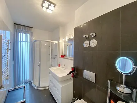 Badezimmer mit ebenerdiger Glasdusche, WC, beheizbaren Handtuchhalter, Fön, Kosmetikspiegel und modernen Waschplatz mit Beleuchtung