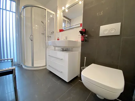 Badezimmer mit ebenerdiger Glasdusche, WC, beheizbaren Handtuchhalter, Fön, Kosmetikspiegel und modernen Waschplatz mit Beleuchtung