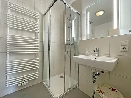 Badezimmer mit Dusche, WC, Kosmetikspiegel, Waschtisch und einem mobilen Wäscheständer