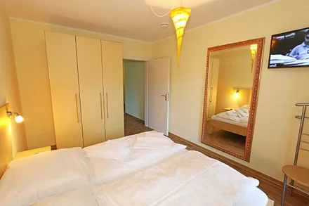 Schlafzimmer mit Doppelbett (1,80 m x 1,90 m), Nachttischkonsolen, Smart-TV, geräumiger Kleiderschrank, großer Wandspiegel und einem Herrendiener mit Sitzmöglichkeit