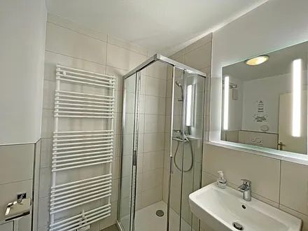 Badezimmer mit Dusche, WC, Kosmetikspiegel, Waschtisch und einem mobilen Wäscheständer