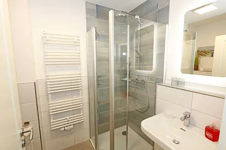 Badezimmer mit Glasdusche (niedriger Einstieg), Waschplatz, WC, Kosmetikspiegel, Fön und Handtuchtrockner