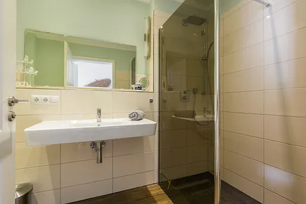 Badezimmer mit ebenerdiger Dusche, Waschbecken, WC, Kosmetikspiegel, beheizbarem Handtuchtrockner, Fön sowie leistungsfähiger Entlüftungsanlage