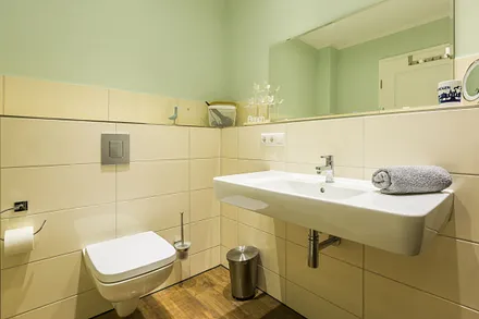 Badezimmer mit ebenerdiger Dusche, Waschbecken, WC, Kosmetikspiegel, beheizbarem Handtuchtrockner, Fön sowie leistungsfähiger Entlüftungsanlage