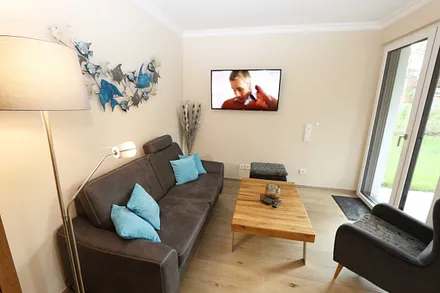 Wohnzimmer mit gemütlicher Couch, Couchtisch, Ohrensesel mit Hocker, Leselampe, Smart-TV, Radio mit CD-Player und Bluetooth/USB sowie eine Vitrine