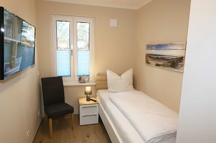 Schlafzimmer mit einem Einzelbett (0,90 m x 2,00 m), Nachttischablage, Kleiderablage, Kleiderschrank und einen weiteren Smart-TV