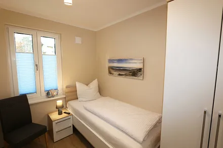 Schlafzimmer mit einem Einzelbett (0,90 m x 2,00 m), Nachttischablage, Kleiderablage, Kleiderschrank und einen weiteren Smart-TV